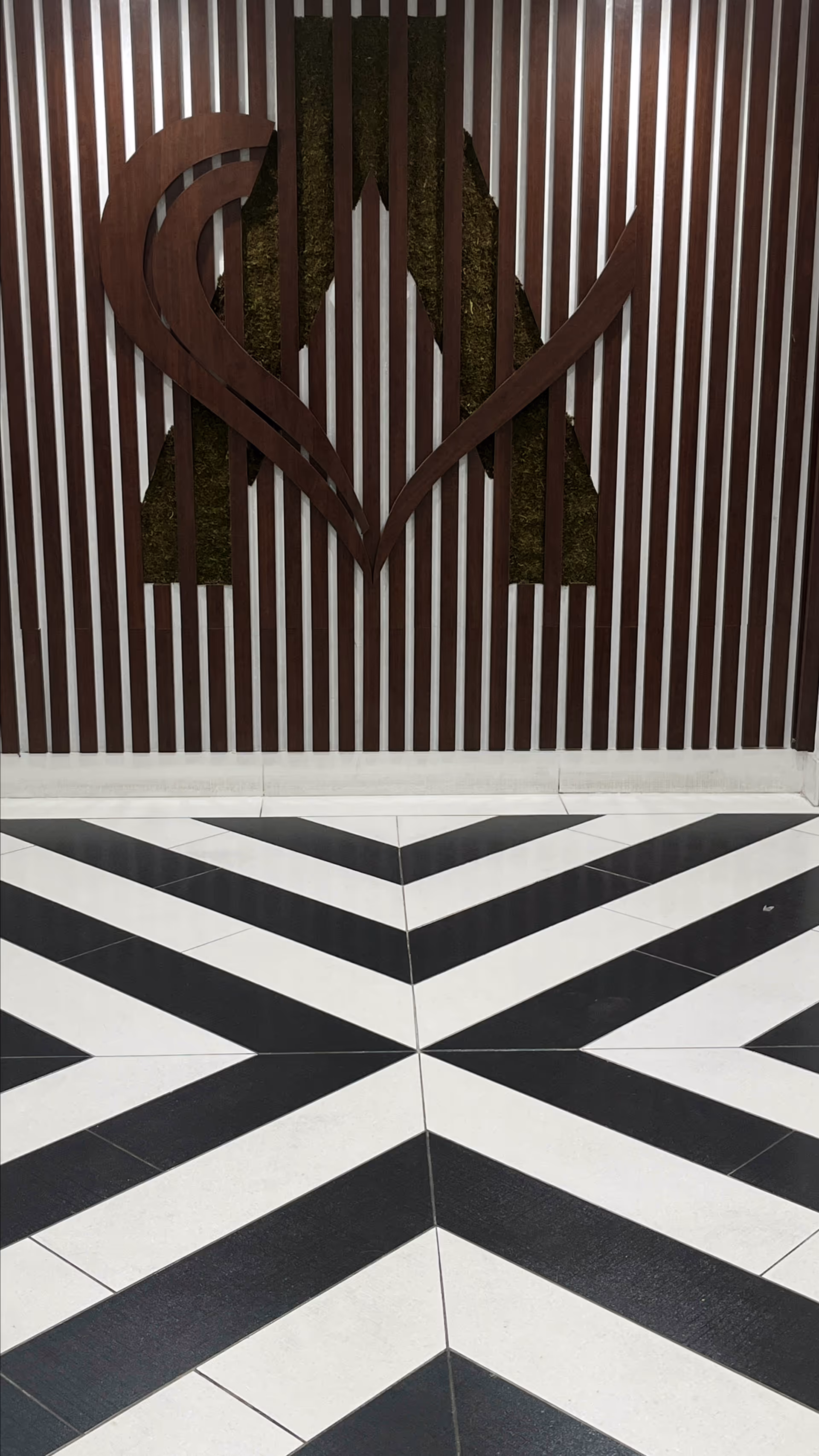 Decorative wall with vertical wooden slats and a large stylized letter A with a heart shape integrated into the design, set above a black and white geometric patterned floor.