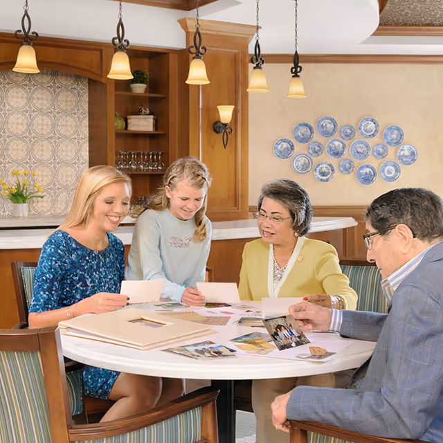 Four adults seated around a round table in a warm communal room looking at photographs and albums.
