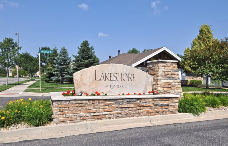 Stone entrance sign reading 'Lakeshore at Centerra' in front of landscaped grounds and a building.