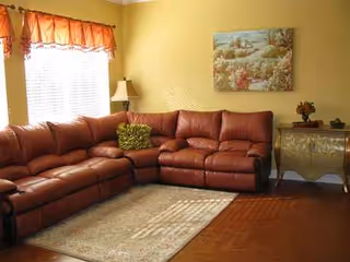 Red leather sectional sofa in a yellow living room with window, lamp, and art.