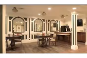 Small dining/common area with round tables and chairs, decorative arched wall panels, a service counter, and warm lighting.