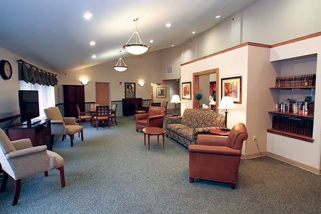 Spacious common lounge with sofas, armchairs, tables, lamps, a TV, and bookshelves.