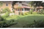 Grassy courtyard garden with plants and a multi-story building and covered walkway in the background.
