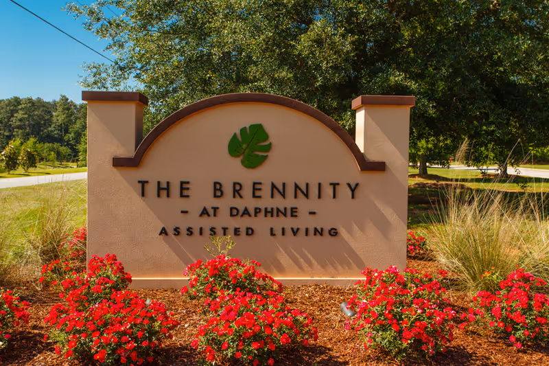 Entrance stone sign for The Brennity at Daphne Assisted Living surrounded by red flowers and landscaping.