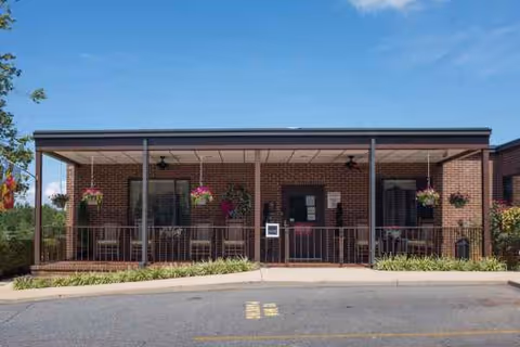 Brick senior living facility with a covered front porch and hanging flower baskets.