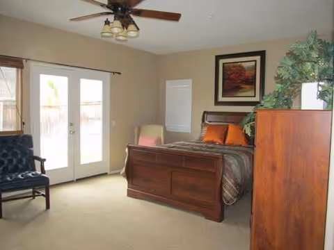 Senior living bedroom with wooden bed, dresser, chair, and double glass doors.