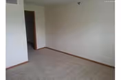 Empty room with beige carpet, white walls, and wooden baseboards. There is an open doorway leading to another room.