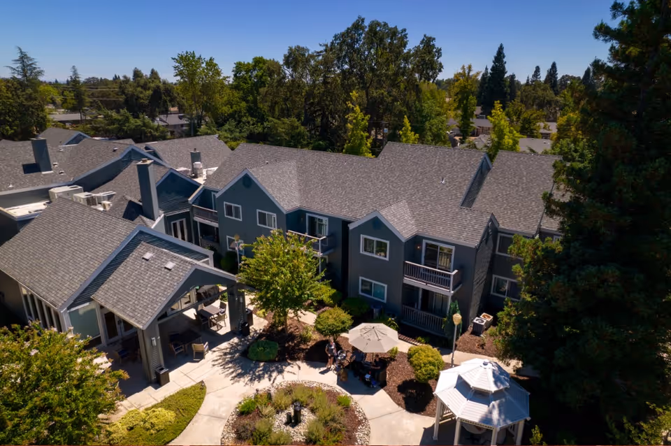 Aerial view of a gray multi-unit senior living building surrounding a landscaped courtyard with seating, umbrellas and a gazebo.