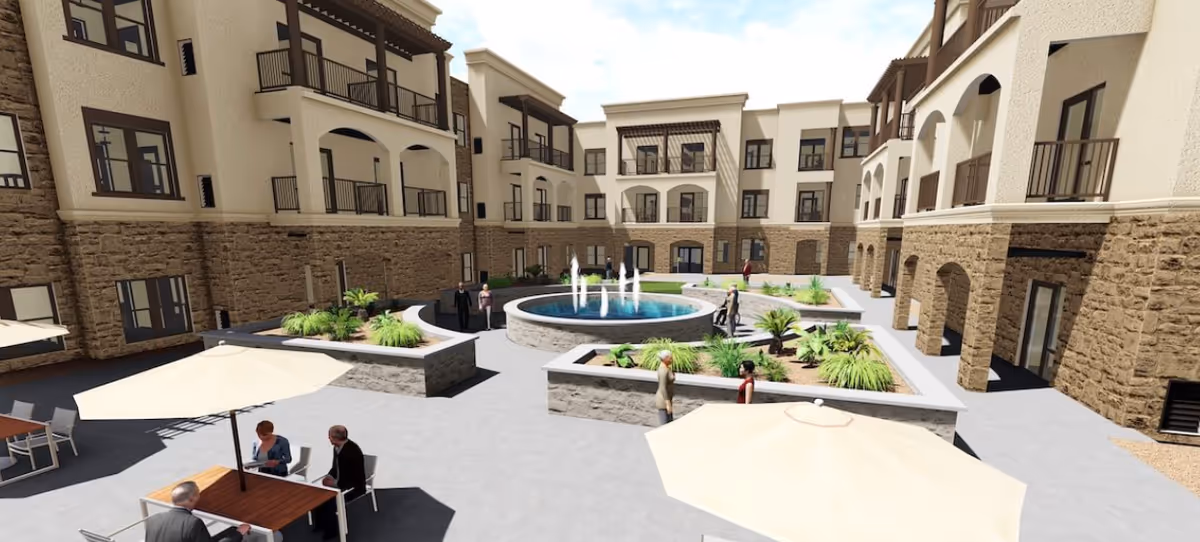 Sunlit central courtyard of a multi-story senior living building featuring a circular fountain, raised planters, balconies, and outdoor seating with umbrellas.