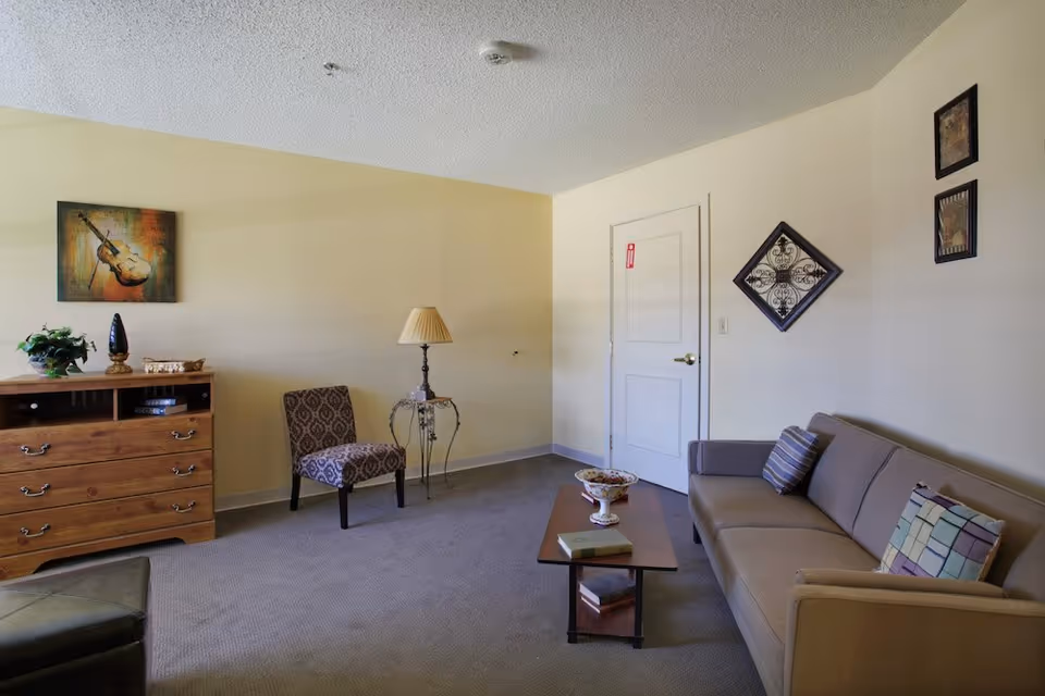 A tidy living room with a sofa, coffee table, accent chair, wooden dresser and wall decorations.