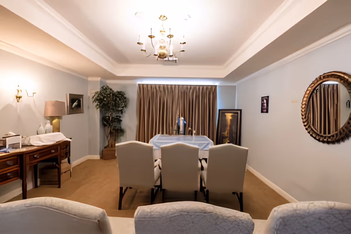 Dining room with a table surrounded by upholstered chairs, a chandelier, sideboard, and wall mirror.