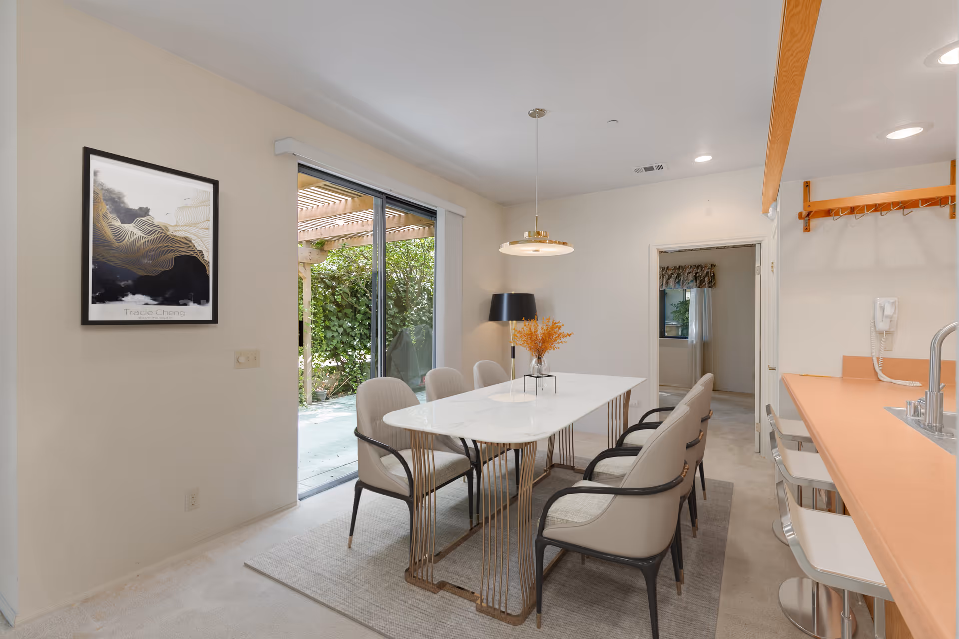 Bright dining room with a long white table and six chairs beside sliding glass doors leading to a patio.