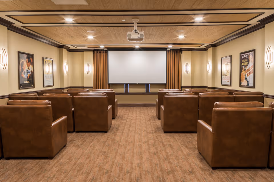 A cozy screening room with rows of brown leather armchairs facing a projector screen and movie posters on the walls.