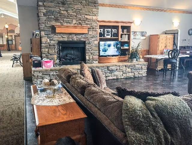 Cozy communal living room with a brown sectional sofa facing a stone fireplace and a built-in TV and shelving.