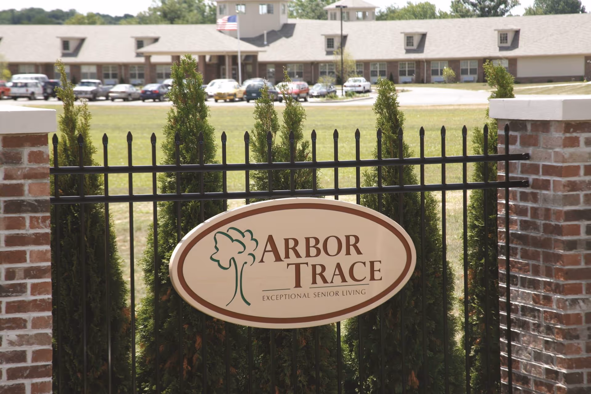 Gated entry with Arbor Trace Senior Living sign and long building façade in background.