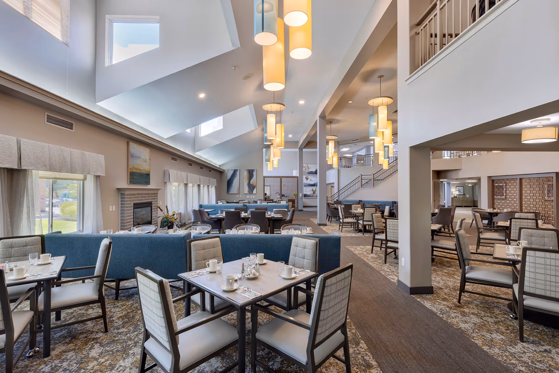 Spacious, well-lit dining room with multiple tables and chairs, high vaulted ceilings, pendant lights, and lounge seating.