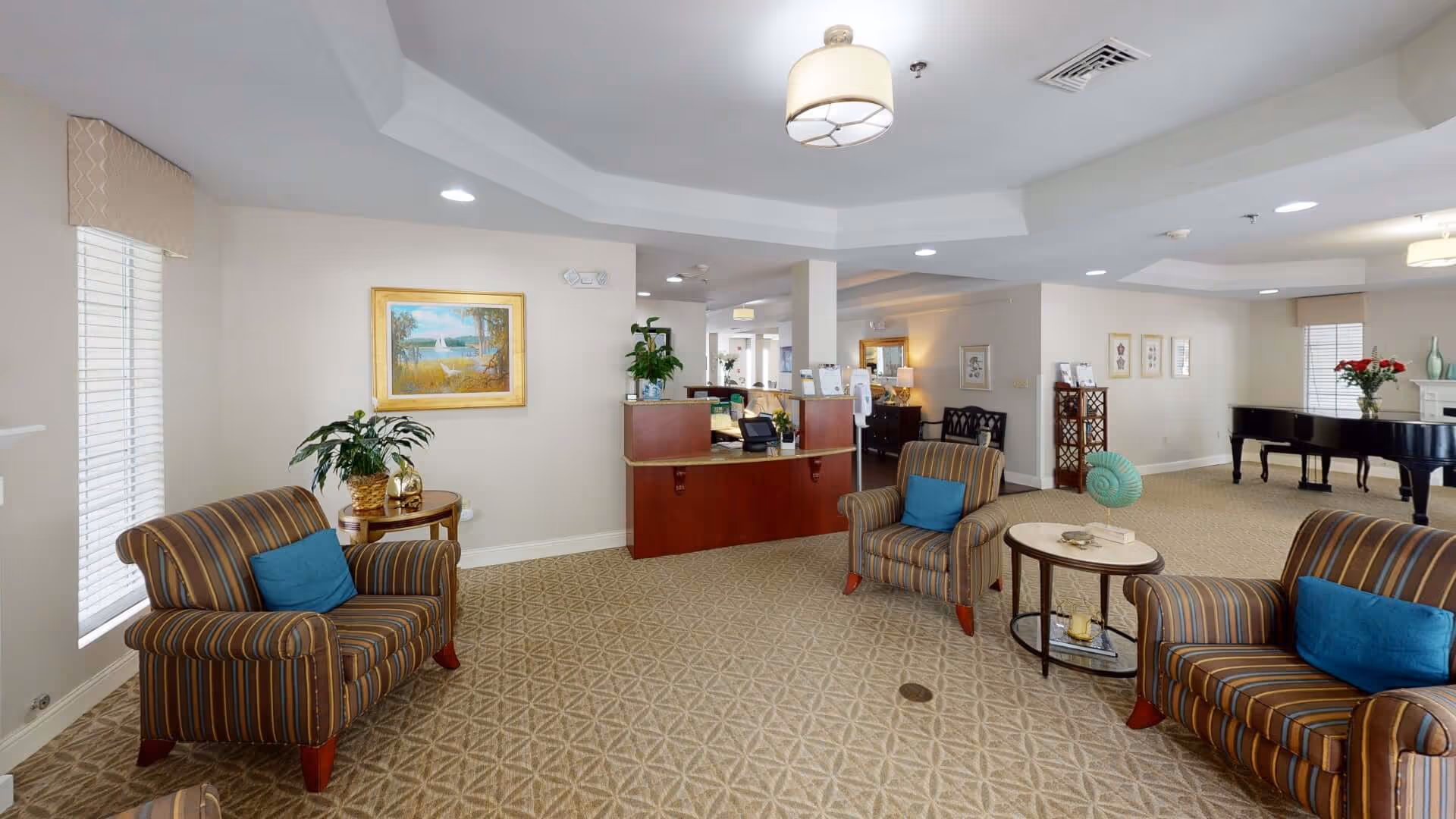 Lobby-style common area with a reception desk, striped armchairs with blue pillows, side tables, and a piano.