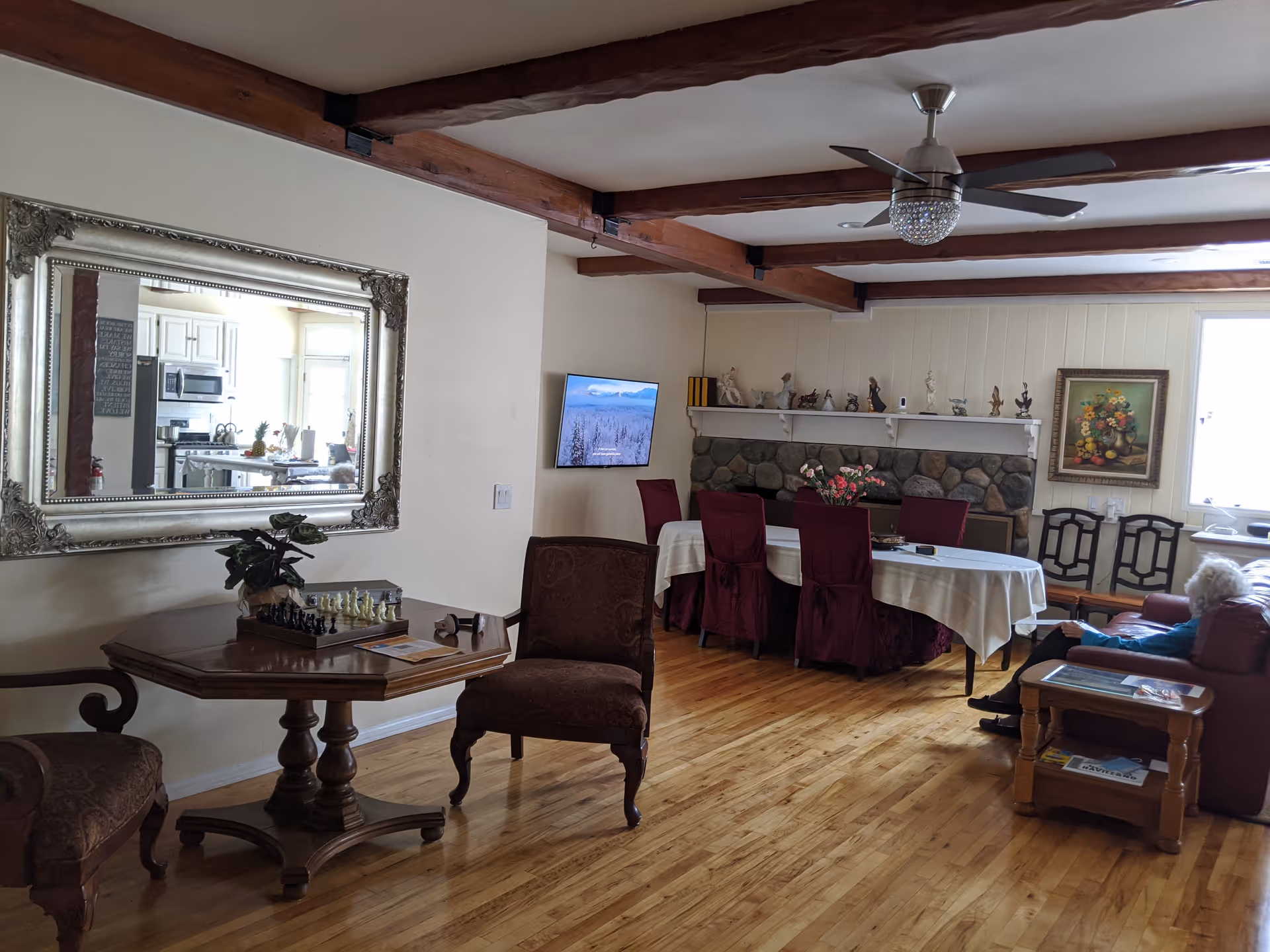 Communal living and dining area with a long table and chairs, stone fireplace, seating, and decorative mirror.