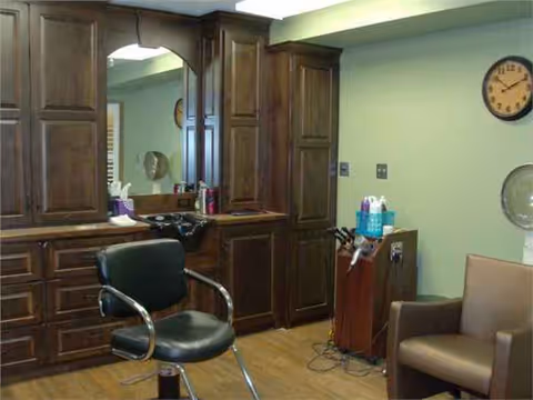 Barber station with dark wooden cabinets, mirror, and black salon chair in a pastel-colored room.