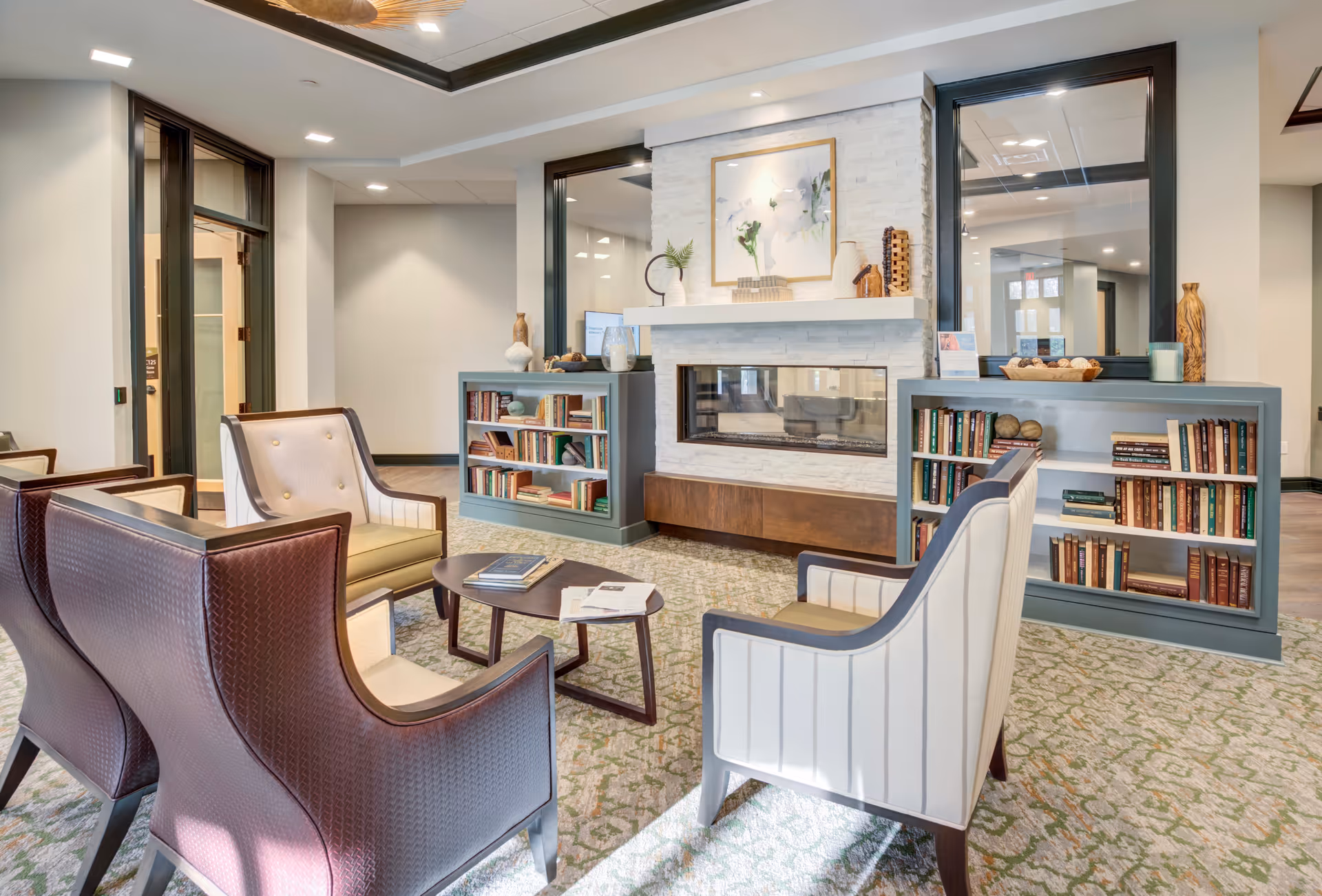 Cozy seating area with armchairs arranged around a coffee table facing a fireplace flanked by bookshelves in a lounge.
