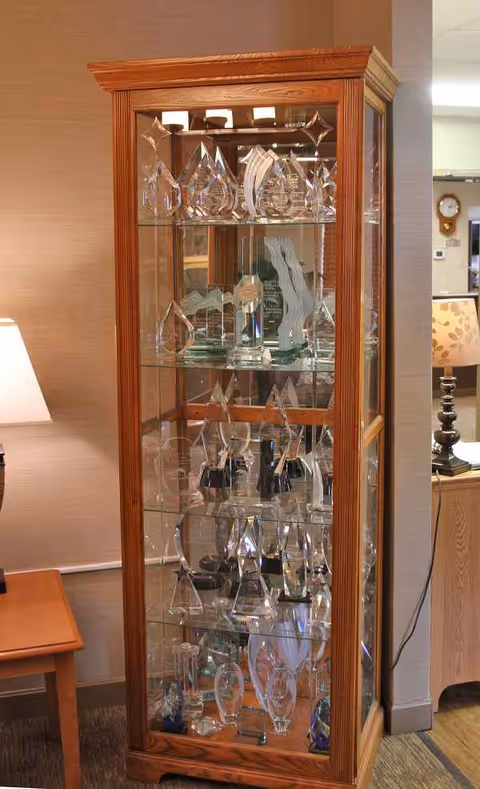 Wooden glass display cabinet filled with crystal awards in a lobby corner.
