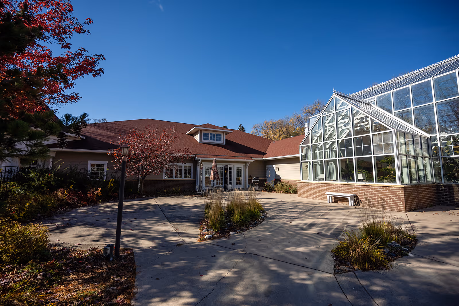 Courtyard and entrance of a low brick building with a red roof and attached glass greenhouse under a clear blue sky.
