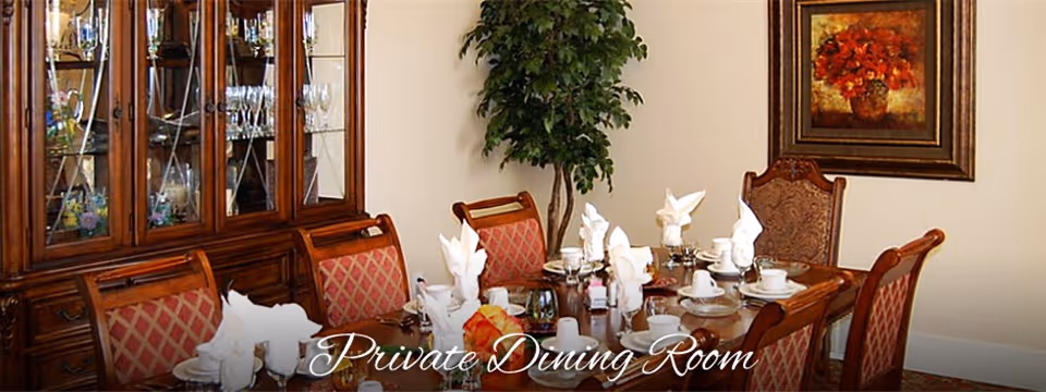 A private dining room with a wooden dining table set for a meal, including white napkins folded elegantly, cups, plates, and silverware. The room features upholstered chairs with a red and gold pattern, a large wooden china cabinet filled with glassware, a potted plant in the corner, and a framed painting of red flowers on the wall.