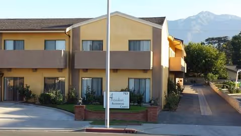 Two-story beige retirement center with balconies, a front sign, and a driveway.