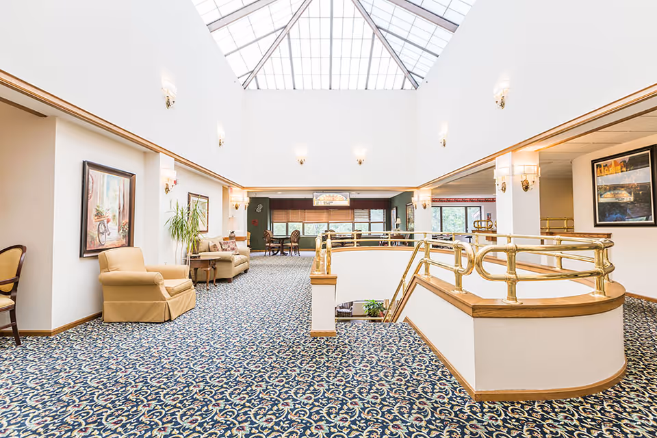 Bright atrium-style common area with patterned carpet, seating, a large skylight, and brass railings overlooking a lower level.
