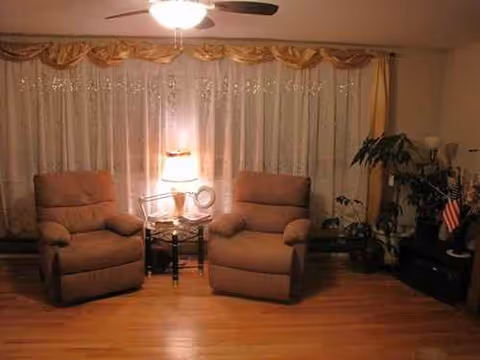 Two beige armchairs flank a small table with a lamp in a cozy living room.