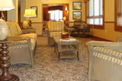 Cozy common sitting area with upholstered chairs, a coffee table, lamps, and large windows.