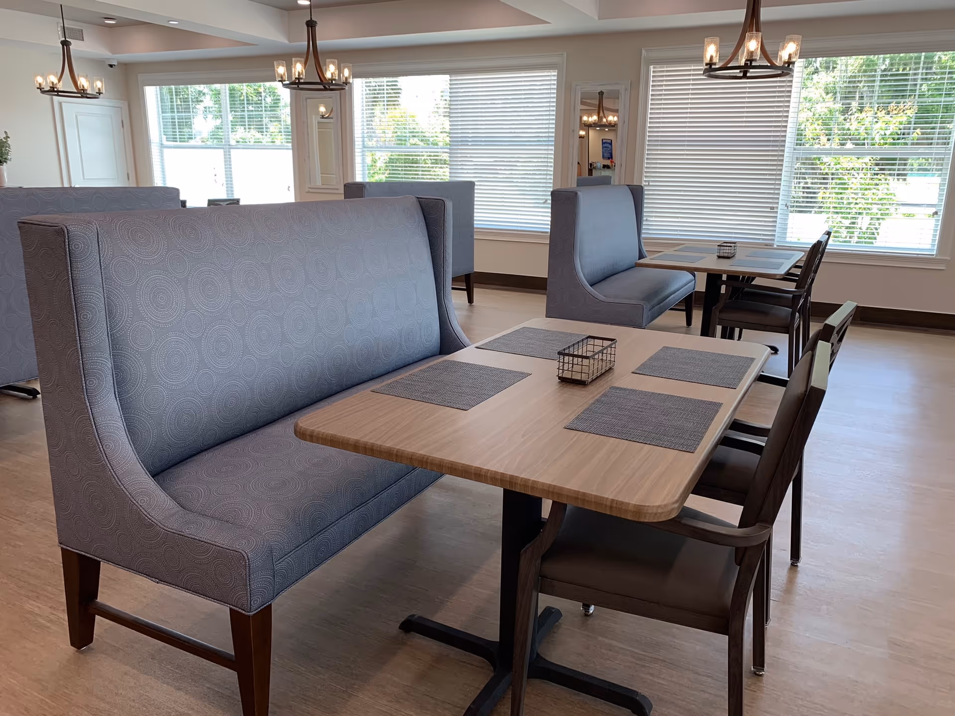 Bright dining room with upholstered booth seating and tables arranged near large windows.