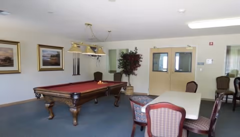 Recreation room featuring a red-felt pool table, overhead lights, and seating with tables and chairs.