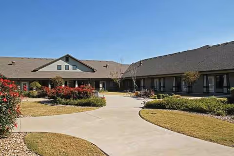 Exterior view of Stonefield Assisted Living building with curved walkway and landscaped courtyard