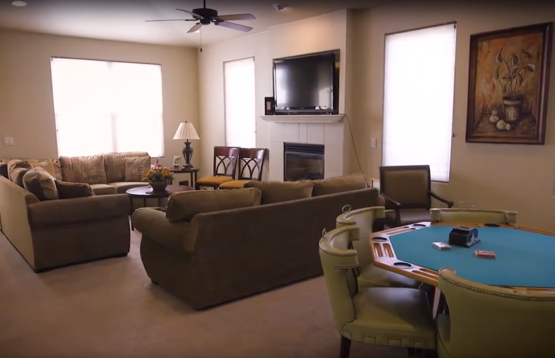 A bright communal living room with sofas, a TV above a fireplace, and a poker table with chairs.