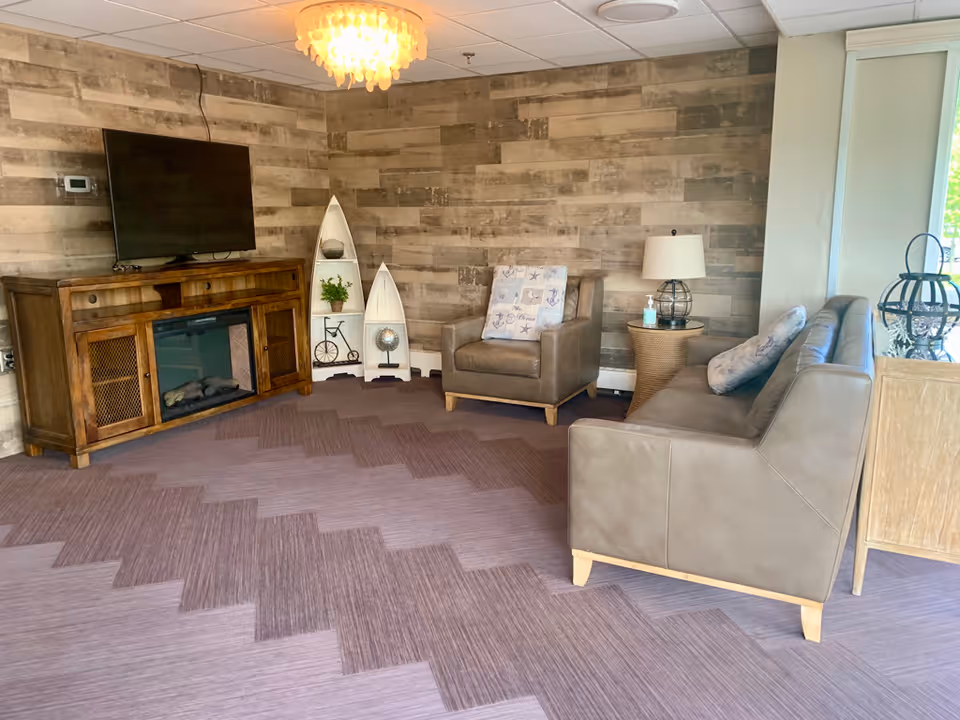 A cozy lounge with a sofa and armchair, a TV on a wooden console, decorative boat-shaped shelves and a lamp against a wood-paneled wall.