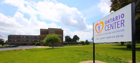 Exterior view of Ontario Center sign beside a low brick building on green lawn.