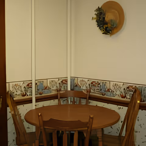 Small dining nook with a round wooden table and chairs, a decorative wallpaper border, and a hat hanging on the wall.