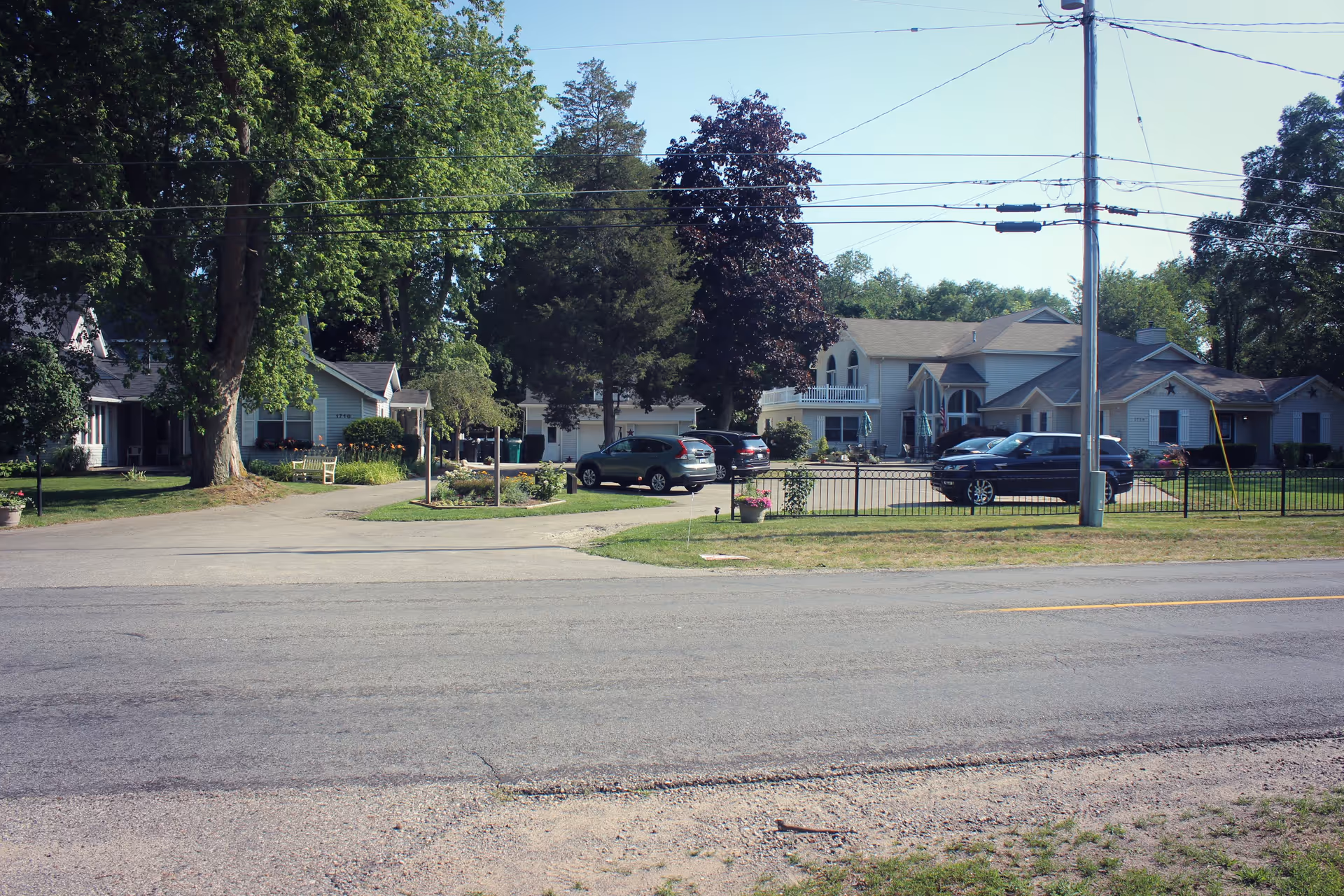 Front view of the Care Cardinal Macatawa complex showing connected buildings, parked cars, lawns and large trees across a street.