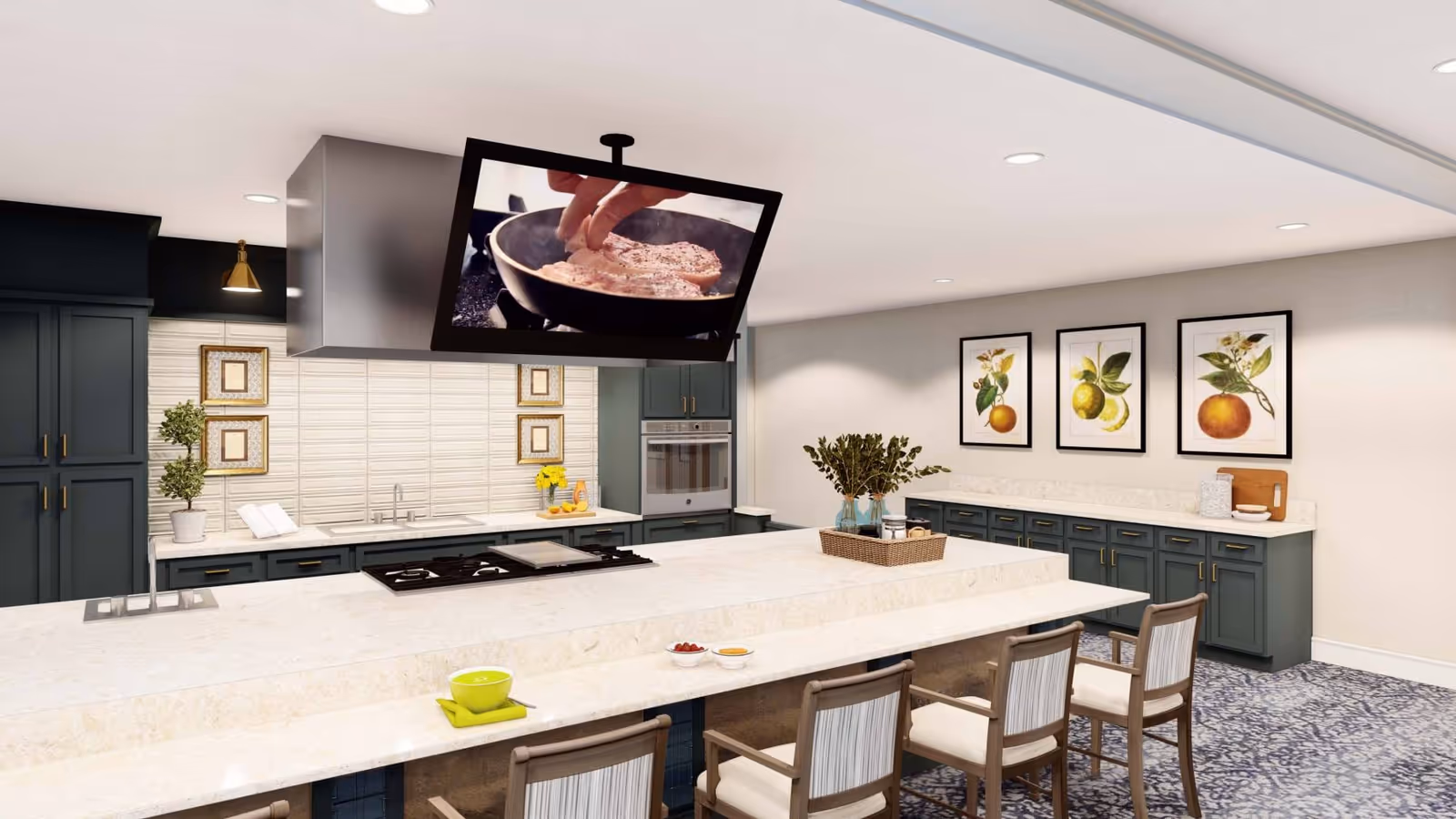 Bright communal kitchen with a long marble island, bar stools, a hanging TV over a cooktop, and dark green cabinetry.