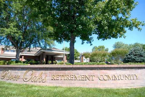 River Oaks Retirement Community sign along a brick wall with trees and a building behind