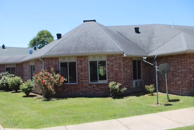 Single-story brick care facility exterior with a lawn, shrubs, sidewalk and a satellite dish.