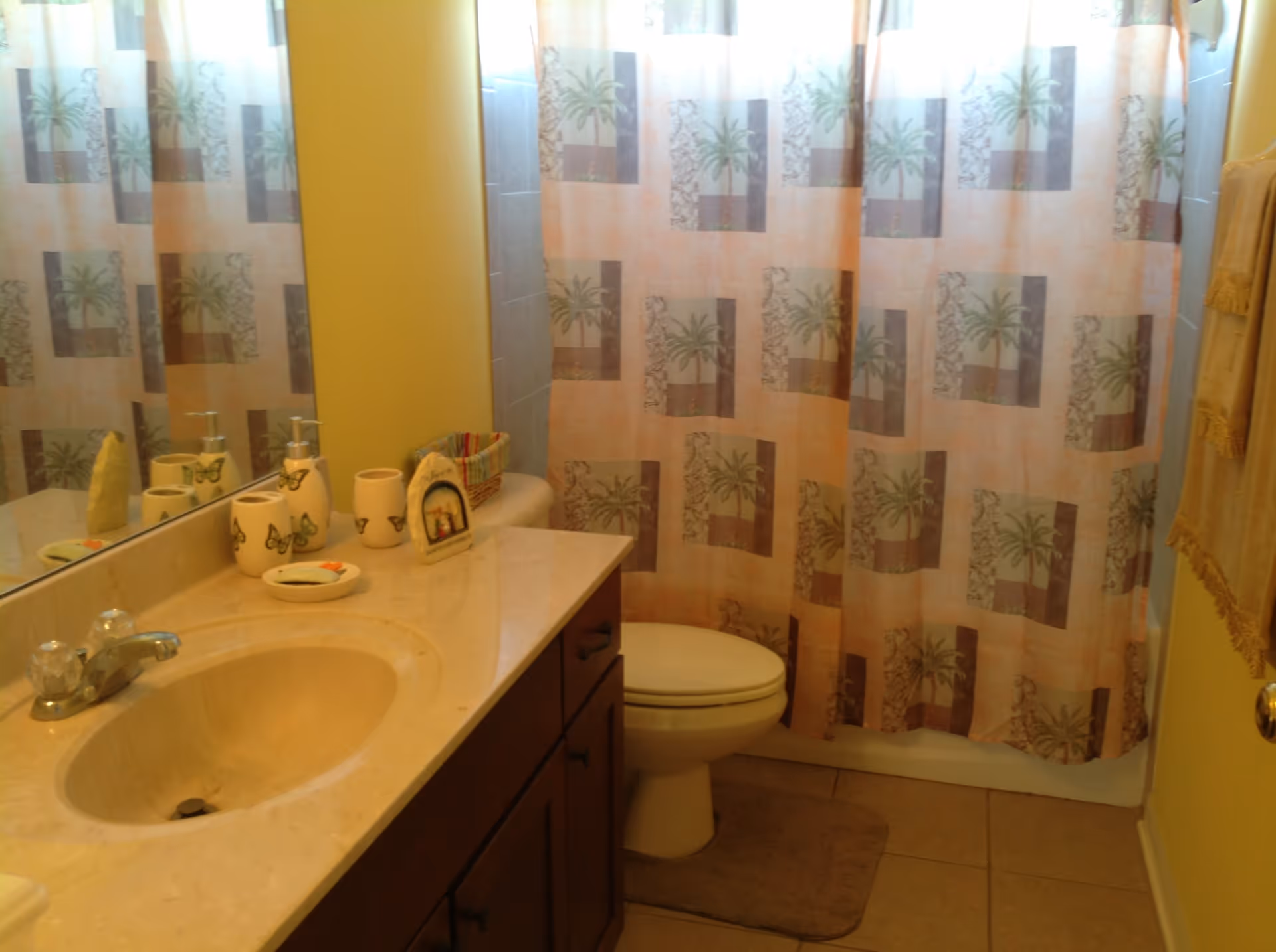 Bathroom with a sink and countertop, toilet, and a palm-patterned shower curtain.