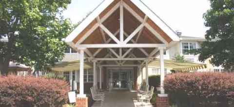 Covered entrance to Brookdale Northampton with benches, shrubs, and a walkway.