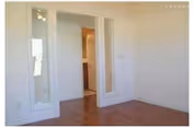 Empty room with hardwood floors, white walls, mirrored closet doors, and an open doorway leading to a bathroom.