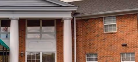 Brick senior living facility exterior with white columns and large front windows.