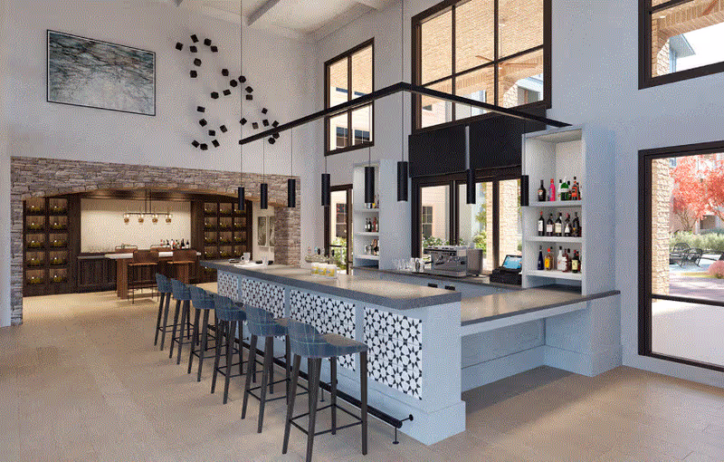 Modern indoor bar area with a long counter featuring patterned panels, several high stools, and shelves stocked with bottles. Large windows provide natural light and a view of an outdoor patio with trees. The space has high ceilings, pendant lights, and a stone accent wall with additional seating and wine storage in the background.