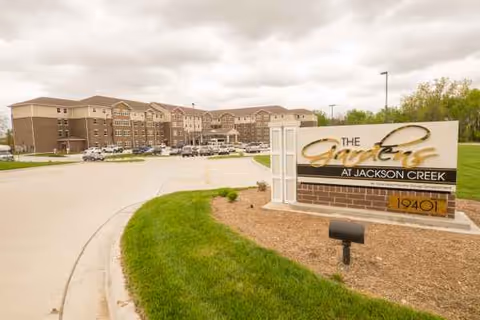 Exterior view of The Gardens at Jackson Creek facility with sign and parked cars.
