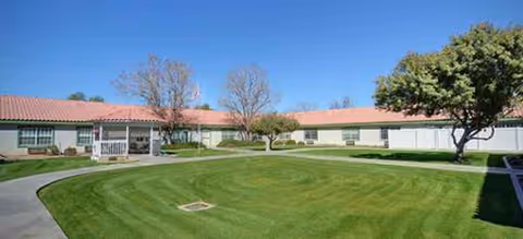 Exterior view of a single-story senior living center with a curved walkway and lawn.