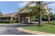 Front view of Optalis Health & Rehabilitation entrance with driveway, lawn, and trees.